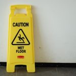 A yellow wet floor caution sign leaning against a white wall.
